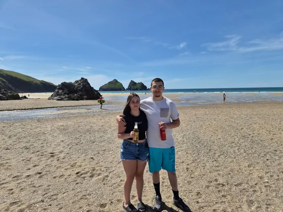 Beach day photo at Holywell Bay with two guests standing on the sand near the sea.