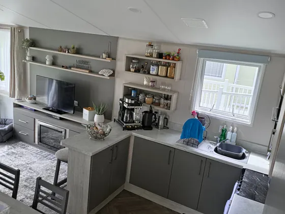 Modern kitchen and lounge area with breakfast bar, shelving and TV.