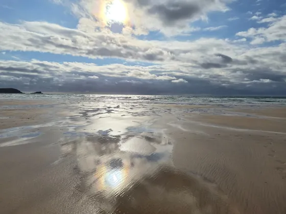 Wide sandy beach with dramatic clouds and reflections on wet sand.